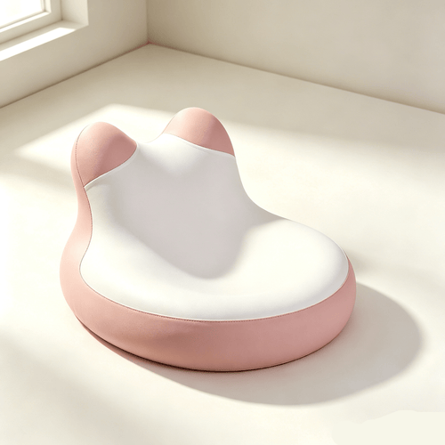 A pink and white cat-shaped lumbar support cushion on a light beige floor in a sunlit room corner.